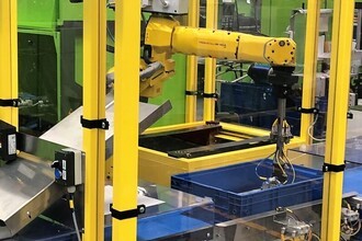 Robot Fanuc M10iA w aplikacji z automatycznym pakowaniem. Do pustych pojemników przemieszczających się taśmociągiem robot pakuje produkty, układając je w określonych kombinacjach.